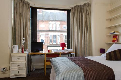 een slaapkamer met een bureau, een bed en een raam bij Campbells Guest House in Leicester