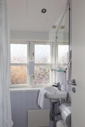 a white bathroom with a sink and two windows at Foldens Hotel Annex in Skagen