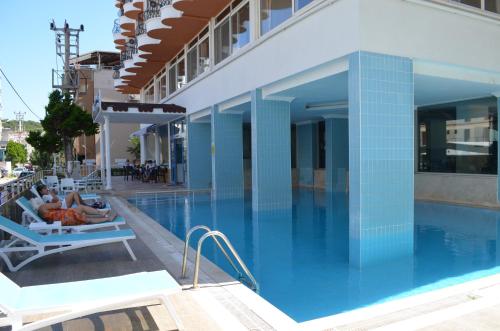 una piscina con 2 personas sentadas en sillas junto a un edificio en Grand Milano Hotel en Ayvalık
