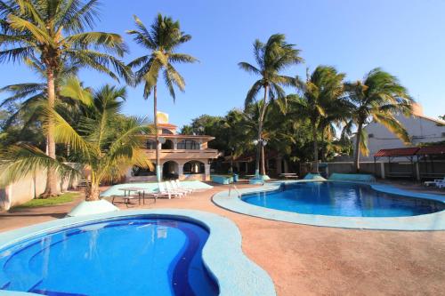 a swimming pool with palm trees and a house at Hotel Gran Palmeiras in Chachalacas