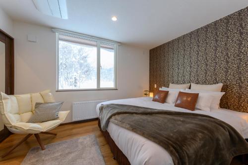 a bedroom with a bed and a chair and a window at SnowDog Village in Niseko