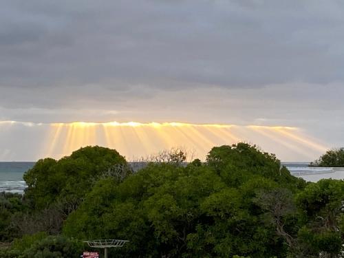 a rainbow in the sky over the ocean with trees at Sea Jewel in Pearly Beach