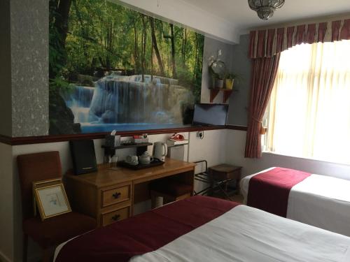 a room with two beds and a desk with a waterfall painting on the wall at The Nyton Guesthouse in Ely