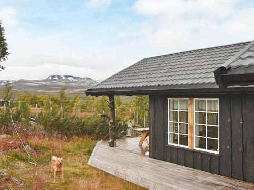 uma pequena cabana preta com um cão de pé num convés em 6 person holiday home in Rennebu em Sundset