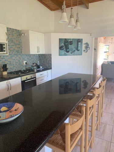 a kitchen with a black counter top and wooden chairs at Hemel-en-See Beach House in Hermanus