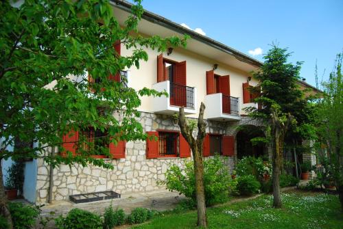 a house with red shuttered windows and trees at Hotel Faraggi in Kleidonia