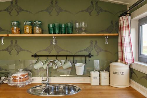 a kitchen counter with a sink and a shelf with cups at The Covey in Felbrigg