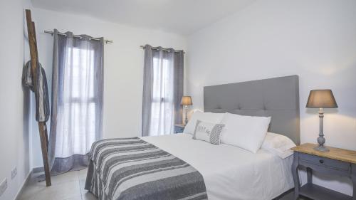 a white bedroom with a bed and a table with a lamp at Marea Fuerteventura Home in Corralejo