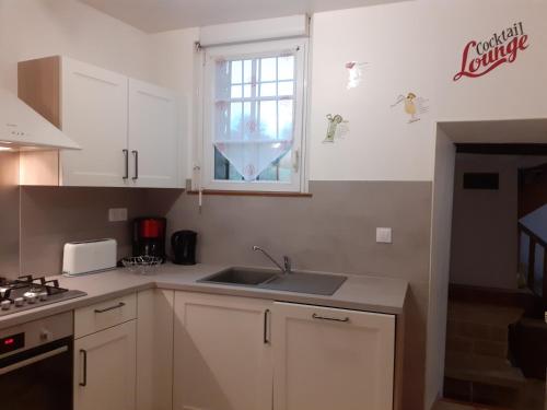 a kitchen with white cabinets and a sink and a window at Gîte de la Ferme de la Côte in Les Damps