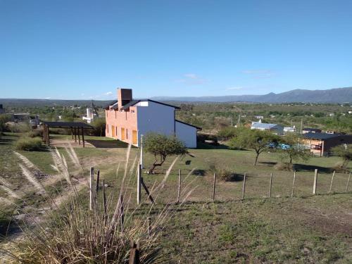 un bâtiment dans un champ avec une clôture au premier plan dans l'établissement Complejo Acanto, à Villa Carlos Paz