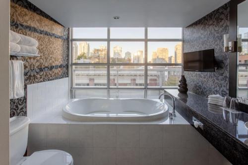 バンクーバーにあるOPUS Vancouverのバスルーム(バスタブ、トイレ付)、窓が備わります。