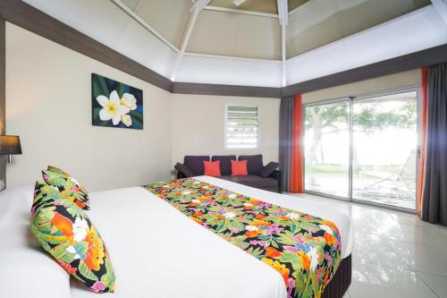 - une chambre avec un grand lit blanc et une couverture colorée dans l'établissement Hotel Koulnoue Village, à Hienghène