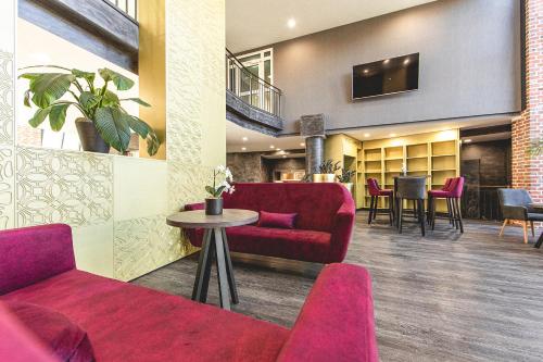 vestíbulo con sofá rojo, mesa y sillas en PLAZA Premium Parkhotel Norderstedt, en Norderstedt