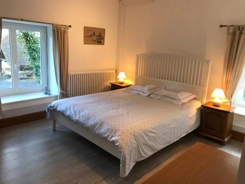 ein Schlafzimmer mit einem Bett mit zwei Nachttischen und zwei Fenstern in der Unterkunft Beautiful Country House with Yoga Studio in Feugères