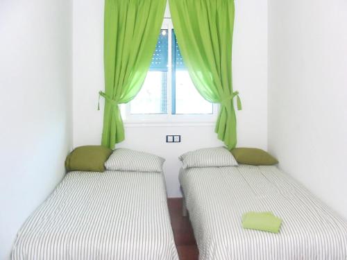 zwei Betten in einem Zimmer mit einem Fenster mit grünen Vorhängen in der Unterkunft Bright apartment in Alcanar with sea and mountain views in Les Cases d'Alcanar