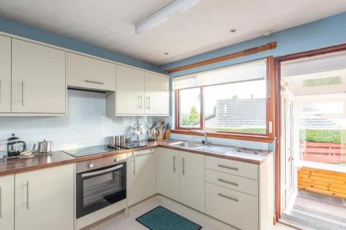 a kitchen with white cabinets and a large window at 2 Bed home with private garden in the Highlands in Beauly