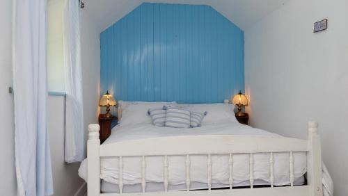 a white bed with a blue headboard in a bedroom at Cosy & Quirky Cottage nr Kynance cove in Lizard