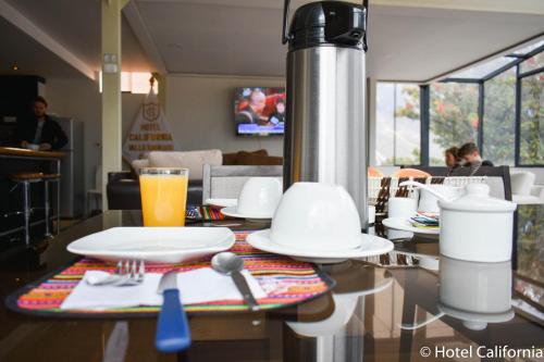 a table with plates and a glass of orange juice at Hotel California Calca in Calca