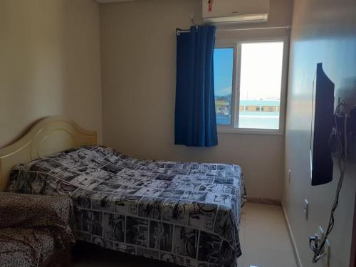 - une chambre avec un lit doté d'un rideau bleu et d'une fenêtre dans l'établissement Edificio Freitas, à Imbituba