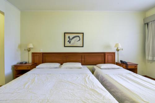 a bedroom with two beds and two tables and a picture on the wall at Park Tower Campinas Residence by Nacional Inn in Campinas