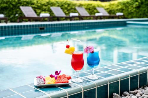 two cocktails and a plate of food next to a swimming pool at The Airport Courtyard Suvarnabhumi Airport in Bangkok