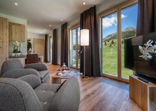 uma sala de estar com sofás e uma televisão e janelas grandes em Golf- & Sporthotel Hof Maran em Arosa