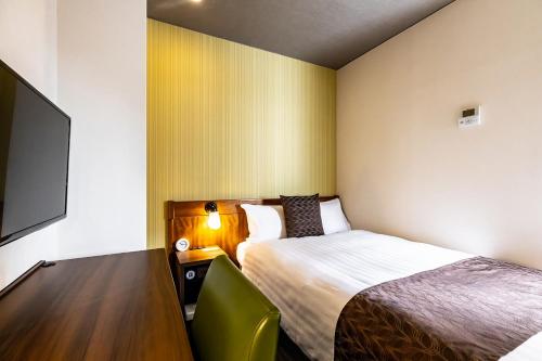 a hotel room with a bed and a desk with a tv at Hotel Quest Shimizu in Shizuoka