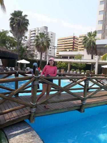 une femme assise sur une clôture à côté d'une piscine dans l'établissement SUITES LE JARDIN CALDAS NOVAS, à Caldas Novas