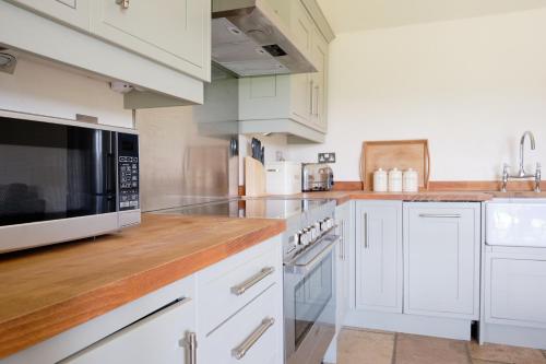 a kitchen with white cabinets and a black microwave at Barn Owl Lodge at Millfields Farm Cottages in Ashbourne