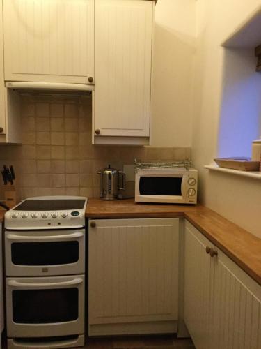 a kitchen with white cabinets and a stove and a microwave at Swallow Barn at Millfields Farm Cottages in Ashbourne