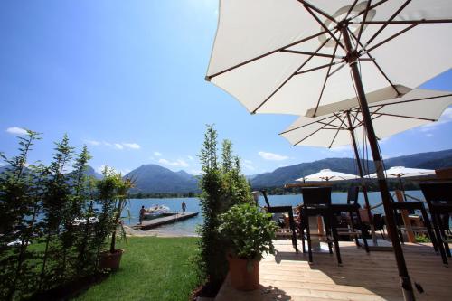 a patio with a table and an umbrella and a body of water at Hotel Seehang Garni in St. Wolfgang