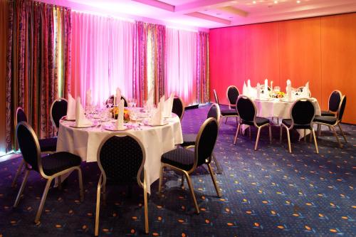 a conference room with tables and chairs and pink curtains at H+ Hotel & SPA Friedrichroda in Friedrichroda
