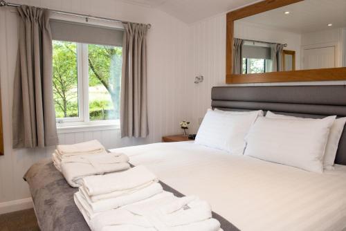 een slaapkamer met een bed met witte kussens en een spiegel bij Luxurious Super-king Lodge with hot tub in Langbank
