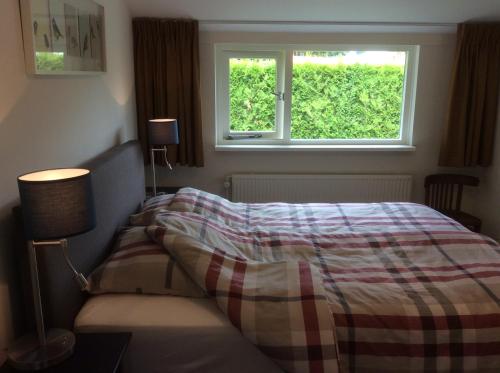 ein Schlafzimmer mit einem Bett mit einer karierten Decke und einem Fenster in der Unterkunft Vakantiehuisje vlakbij de duinen in Oostvoorne