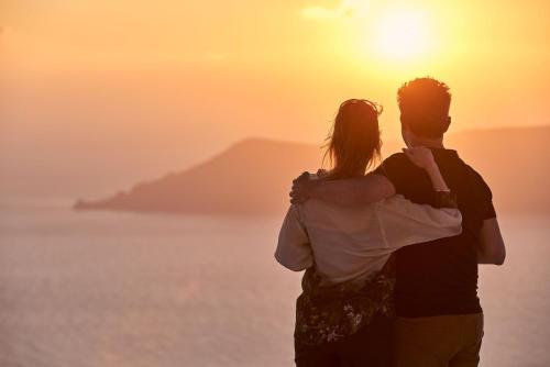 a man and woman standing on the beach watching the sunset at Astra Suites in Imerovigli
