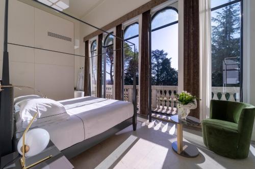 a bedroom with a bed and a chair and windows at Hotel Villa Soligo - Small Luxury Hotels of the World in Farra di Soligo