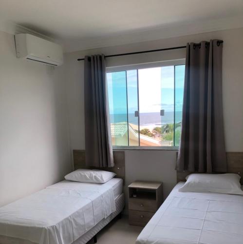 two beds in a room with a large window at Residencial Galápagos in Imbituba