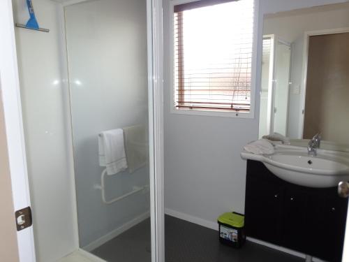 a white bathroom with a sink and a shower at Kauri Lodge Karapiro in Karapiro