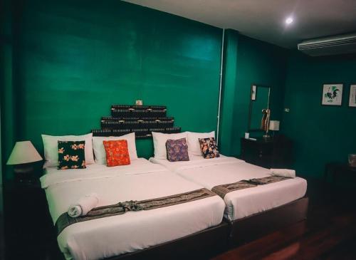 a green room with a large bed with pillows at Thaweesuk Heritage Homestay in Phangnga