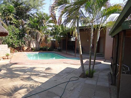 a swimming pool with palm trees next to a house at Lephalale Guest House in Ellisras