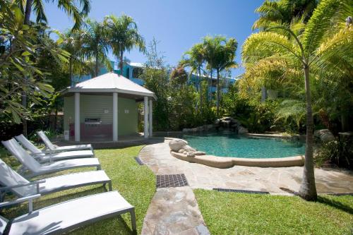 uma piscina com espreguiçadeiras brancas num quintal em Verandahs Boutique Apartments em Port Douglas