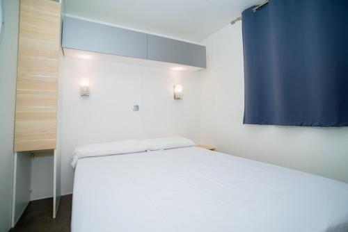 a bedroom with a white bed and a blue curtain at Camping Joncar Mar in Roses