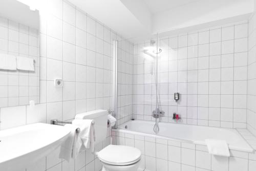 La salle de bains blanche est pourvue de toilettes et d'une baignoire. dans l'établissement Hotel Motodrom, à Hockenheim