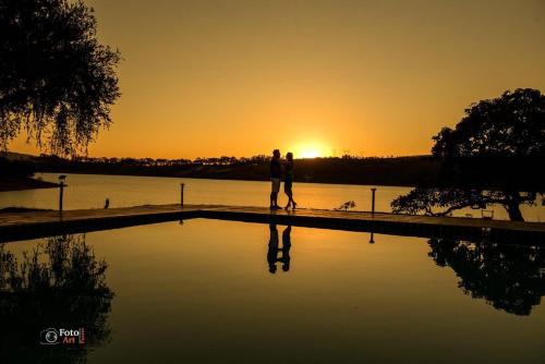 a couple standing next to a swimming pool at sunset at Pousada Recanto do Turvo in Capitólio