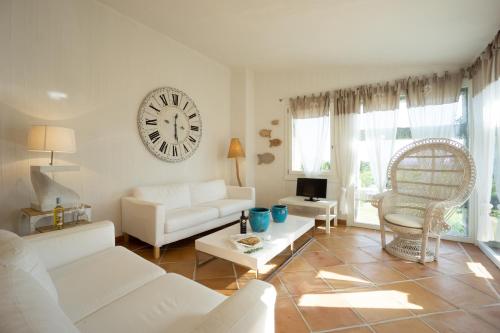 a living room with white furniture and a clock on the wall at BGItalianVacation - Ville Li Conchi in Castiadas