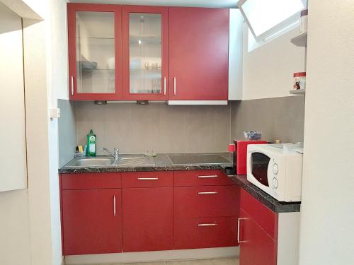 a red kitchen with a sink and a microwave at Comfortable studio in Bevaix with mountain view - 30 m² + Spa in Bevaix