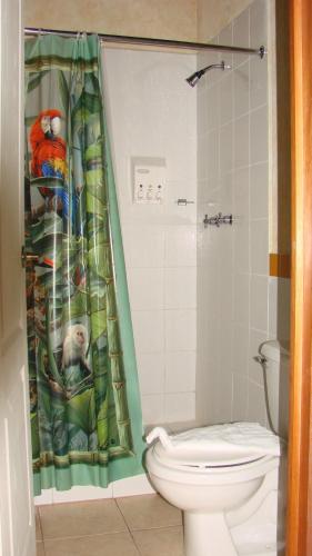 a bathroom with a toilet and a shower curtain with a parrot at Hotel Bahia Taitza in Flores