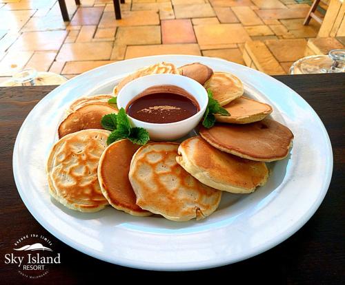 a plate of pancakes with a bowl of syrup at Sky Island Resort in Ponta Malongane