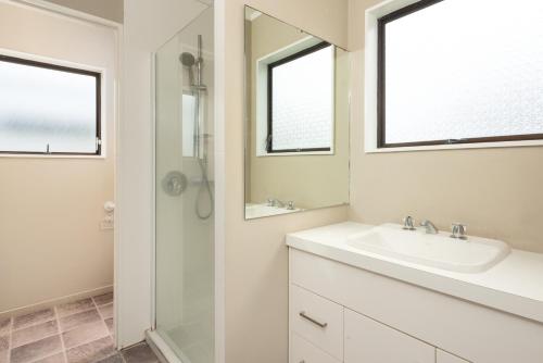 a white bathroom with a sink and a mirror at The Mount Beach Pad - Mt Maunganui Holiday Home in Matapihi