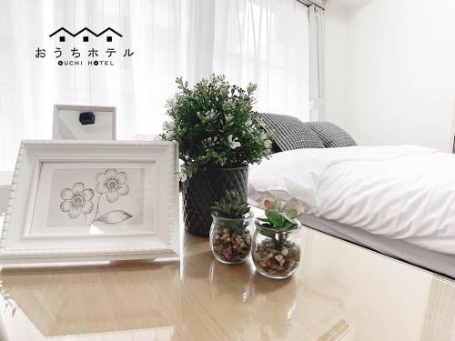 a table with potted plants and a picture and a bed at OUCHI HOTEL Takaramachi in Hiroshima